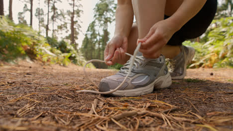 Primer-Plano-De-Una-Mujer-Atándose-Los-Cordones-De-Una-Zapatilla-Deportiva-Antes-De-Hacer-Ejercicio-Corriendo-Por-Una-Pista-A-Través-Del-Bosque,-Filmada-En-Tiempo-Real-1